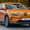 Orange Vinfast VF8 driving on road.
