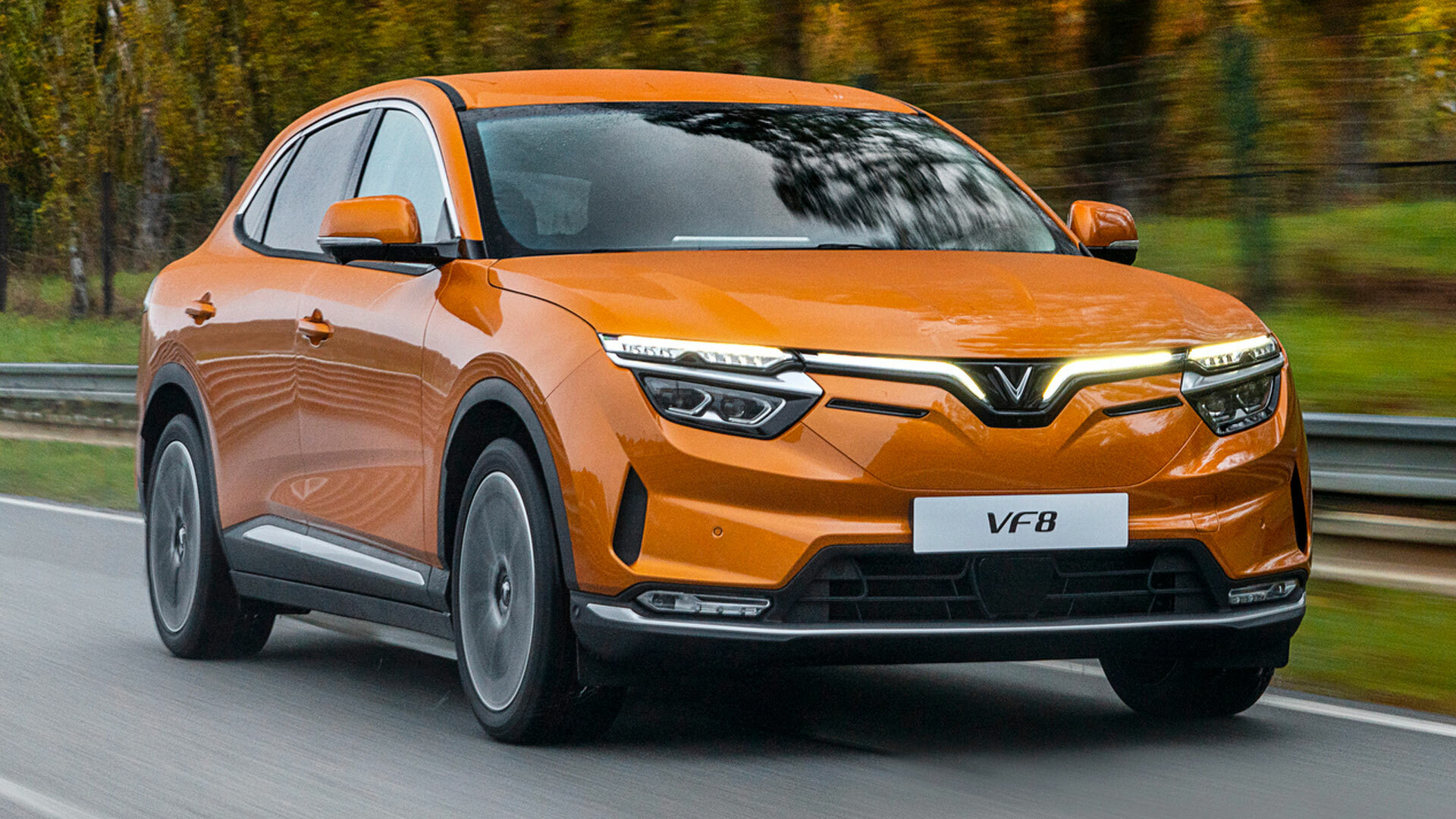 Orange Vinfast VF8 driving on road.