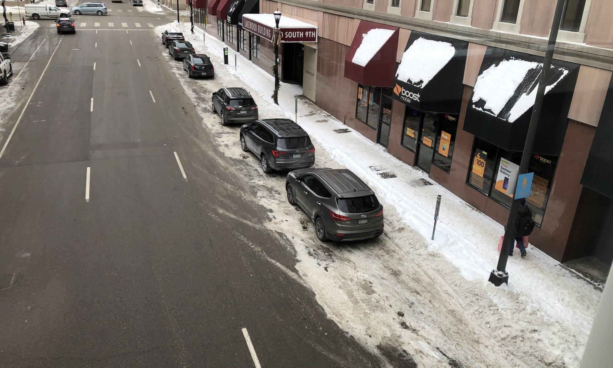 Cars parked on a a neighborhood street by a snow-covered sidewalk